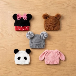 May include: Five knitted beanies featuring animal and character designs. One black with a pink bow and white dots, one brown with round ears, one gray with two pom-poms, one white with black panda features, and one light pink with long floppy ears.
