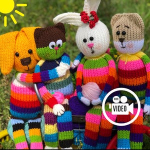 May include: Four handmade, colorful knitted stuffed animals: a yellow dog, a brown cat, a white bunny with red roses, and a tan bear. Each has rainbow striped bodies and are hugging. A ball of pink yarn is in the bunny's arms.
