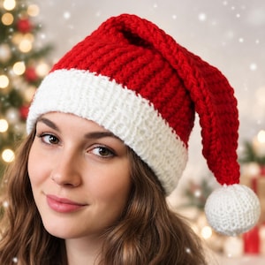 May include: A chunky knit Santa hat featuring a vibrant red main section with a thick, textured white brim and a matching white pom-pom attached to the end of the folded top. The hat is crafted from thick yarn with a visible ribbed stitch pattern.