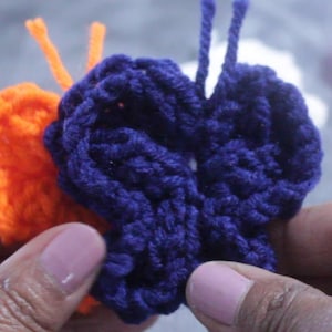 May include: A close-up of a crocheted butterfly with blue and orange yarn. The butterfly is made with a single crochet stitch and has a textured appearance.