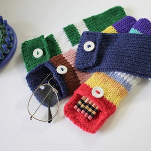 May include: Five knitted pencil cases with different striped patterns and button closures. The cases are filled with pencils, glasses, and other small items.
