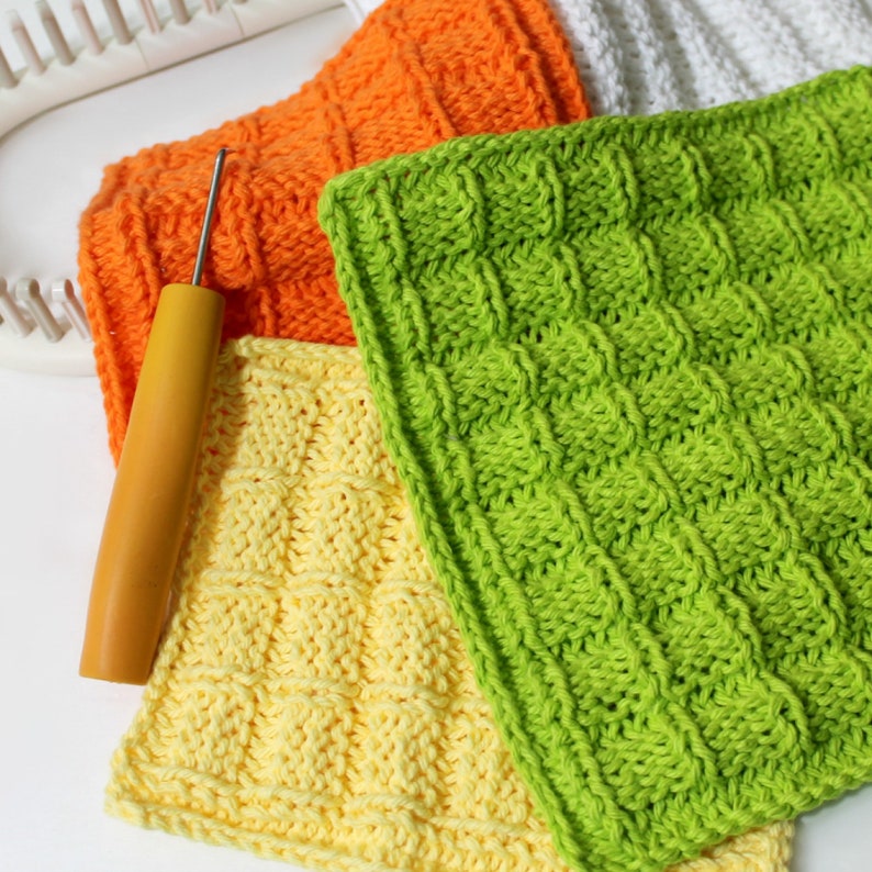 Peut inclure: Plusieurs carr&eacute;s tricot&eacute;s &agrave; la main aux couleurs vives : orange, jaune et vert. Un crochet &agrave; manche en bois repose sur les carr&eacute;s, avec un m&eacute;tier &agrave; tisser blanc en arri&egrave;re-plan. Les carr&eacute;s pr&eacute;sentent un motif textur&eacute; et tiss&eacute;.
