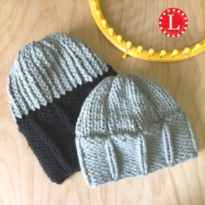 May include: Two knitted beanies. One is grey and black, the other is solid grey. A yellow knitting loom is in the background. A red circle with the letter "L" is visible, indicating size.