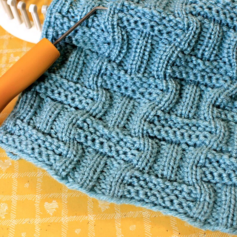 May include: A close-up of a blue knitted fabric with a woven pattern. The fabric is soft and textured, with a subtle sheen.