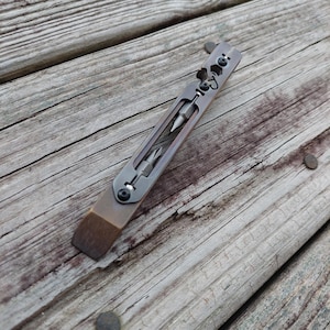 May include: A dark metallic multi-tool pry bar featuring a flat edge, a central cutout housing two interchangeable screwdriver bits, and a series of integrated hex wrench openings secured with small black screws along the upper handle section.