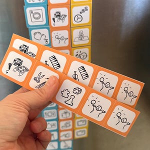 May include: Magnetic tiles with various illustrated icons, including a dog, a washing machine, and a teapot. The tiles are organized into categories labeled "Contribute," "Grow," and "Relax." Additional tiles with musical instruments and other activities are held in a hand.