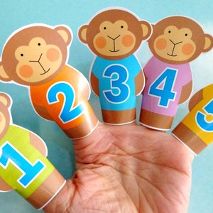 May include: Five finger puppets shaped like monkeys, each wearing a different colored shirt with a number on it. The numbers are 1, 2, 3, 4, and 5.