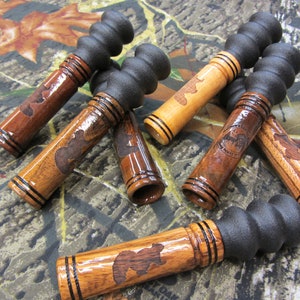 May include: Six wooden duck calls with black rubber mouthpieces. The calls are decorated with a bear silhouette and black trim.
