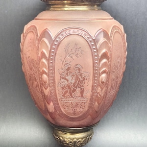 May include: A vintage pink glass hanging lamp with ornate brass accents. The lamp features etched oval panels with classical figures and decorative patterns. A brass chain and decorative top complete the design.