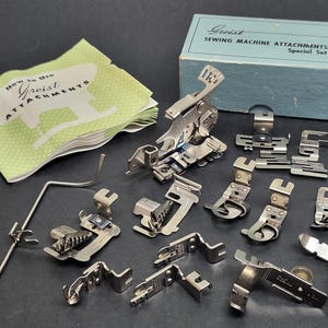 May include: A collection of silver-toned metal sewing machine attachments, including various presser feet and a metal guide bar. The set includes a light blue cardboard box labelled Greist SEWING MACHINE ATTACHMENTS Special Set and a green instruction booklet.