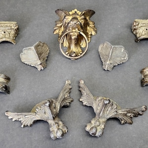 May include: A collection of metallic furniture hardware including a central lion head door knocker with a ring, two ornate winged claw feet, two corner brackets, two small column-style mounts, and two curved decorative accents in a brass finish.
