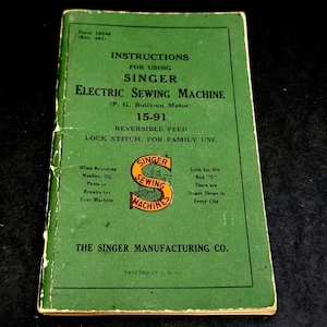 May include: A green instructional manual for a Singer electric sewing machine, model 15-91. The cover features black text, including the title, and a central orange logo with the text Singer Sewing Machines. It is printed in the U.S.A.