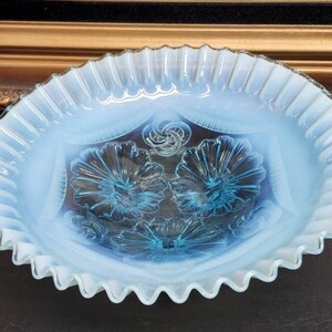 Op de afbeelding: Een ovale, opalescerende glazen kom met een gerimpelde rand. De kom heeft een bloemenontwerp in blauwe en witte tinten. De rand heeft een geschulpte rand.