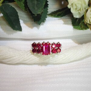 May include: A silver ring with a cluster of red gemstones. The ring features a large, rectangular-shaped red gemstone in the center, surrounded by smaller round red gemstones.