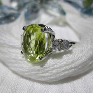Puede incluir: Un anillo de plata con una gran piedra preciosa verde ovalada y dos piedras preciosas redondas transparentes m&aacute;s peque&ntilde;as.