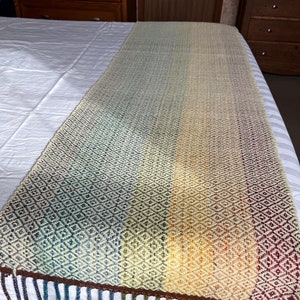 May include: A woven rainbow throw blanket with a diamond pattern and fringe. The blanket is made of natural fibers and has a rustic, handmade look.