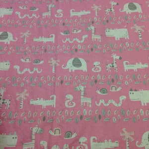 May include: Pink fabric with a repeating pattern of animals, including elephants, giraffes, snakes, and crocodiles. The animals are in shades of gray and white against a pink background.