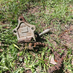 May include: An antique pipe vise with a chain, resting in green grass. The vise is a light green color with the number "11" visible. The chain and vise show signs of age and wear.