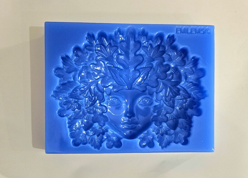 May include: Blue silicone mold with a detailed design of a woman's face surrounded by leaves and acorns. The mold is labeled "EMLEM3C".