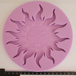Puede incluir: Un molde de silicona morado con forma de sol con cara. El sol tiene los ojos cerrados, una nariz y una boca.