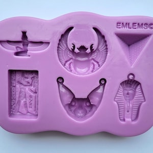 May include: A lilac silicone mould with several Egyptian-themed designs. The mould includes a scarab beetle, a pharaoh, a cat, a pyramid, and other hieroglyphic symbols. The text "EMLEMSO" is visible on the mould.