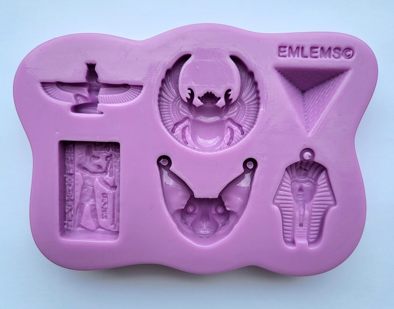 May include: A lilac silicone mould with several Egyptian-themed designs. The mould includes a scarab beetle, a pharaoh, a cat, a pyramid, and other hieroglyphic symbols. The text "EMLEMSO" is visible on the mould.