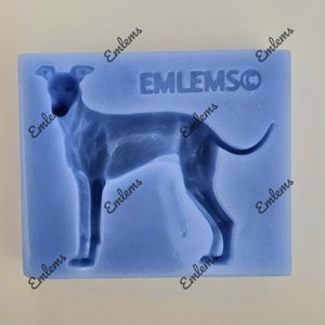 May include: Blue silicone mould for making a dog-shaped cake or other treat. The mould features a detailed outline of a greyhound dog. The mould is labelled "EMLEMSCO".