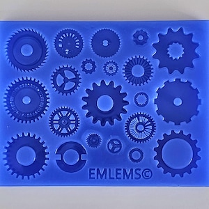 Op de afbeelding: Blauwe siliconen mal met 17 verschillende tandwielvormen, perfect voor het maken van fondant- of marsepeinversieringen. De mal is gemarkeerd met "EMLEMS©".