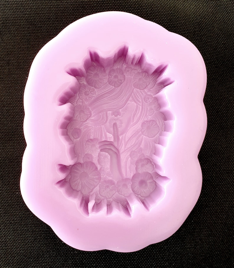 May include: Purple silicone mold with a detailed design of a woman's face with flowers surrounding her. The woman is holding her finger to her lips as if to say "shhh".