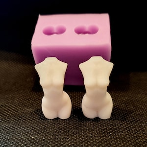 May include: Two white silicone molds for making resin crafts. The molds are shaped like the upper torso of a person. The molds are sitting on a black textured surface.