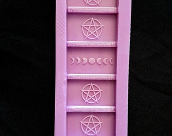 Könnte beinhalten: Eine lilafarbene Silikonform mit fünf Abschnitten. Jeder Abschnitt hat ein anderes Design: ein Pentagramm, eine Mondsichel und ein Pentagramm.