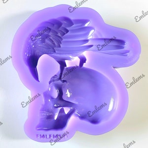 May include: Purple silicone mold of a raven perched on a skull. The mold is for making resin or polymer clay crafts. The mold is labeled "Emblems".