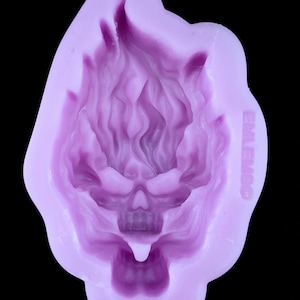 May include: Purple silicone mold for making a skull with flames on top. The mold has the word "EMILENO" on the side.