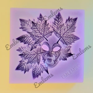 Puede incluir: Molde de silicona morado con un diseño detallado de una máscara de mascarada con hojas. La máscara tiene detalles intrincados y las hojas tienen un delicado patrón de venas. El molde está etiquetado como "Emblems" en la esquina inferior derecha.
