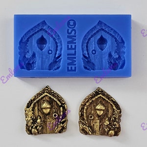 May include: Two gold-coloured resin moulds of a fairy door with an acorn knocker. The moulds are on a blue silicone sheet with the word "EMLEMSCO" printed on it.