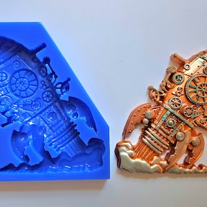 Op de afbeelding: Een blauwe siliconen mal voor het maken van een steampunk-vormig raketvormig harsornament. De mal heeft de vorm van een raket met tandwielen en andere details. Het afgewerkte ornament is te zien op de afbeelding, geschilderd in koper en groen.