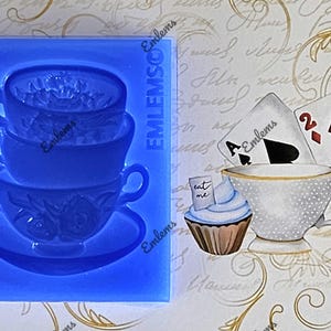 May include: Blue silicone mold of a stack of three teacups and a saucer. The mold is on a white background with a handwritten note and playing cards.
