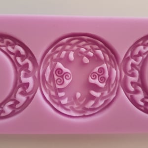 May include: A purple silicone mold with three impressions: two crescent moons with Celtic knot designs and a circle with a Celtic knot design and three triskelions.