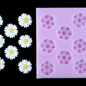 May include: A silicone mold with 10 daisy flower shapes. The mold is pink and the daisy shapes are purple. There are also 10 white daisy flower decorations.