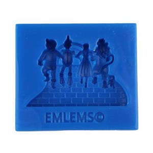 May include: A blue square with a relief of characters from The Wizard of Oz, including the Scarecrow, Tin Man, Dorothy, and the Cowardly Lion. The text "EMLEMSO" is at the bottom.