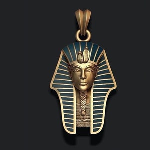 May include: A gold-coloured pendant depicting the bust of an Egyptian pharaoh, with a blue and gold headdress. The pendant has a detailed design and a loop for a chain. The background is a dark grey.