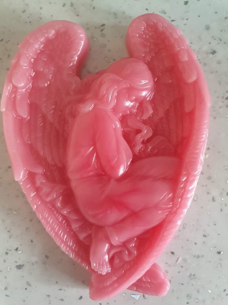 May include: A pink angel figurine with wings outstretched, the angel is kneeling with its head bowed. The figurine is made of a smooth, shiny material.