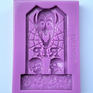 May include: Purple silicone mould for making a Halloween-themed cake topper. The mould features a vampire with fangs, a spiderweb, and the words "RIP".