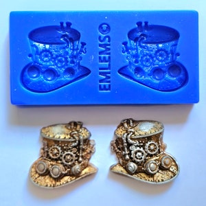 May include: Two gold-colored steampunk-style top hats with intricate details, including gears and goggles. The hats are on a white background.