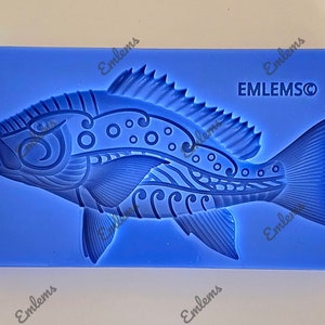 May include: Blue silicone mold with a detailed design of a fish with a stylized pattern. The mold is for making decorative items or edible treats.