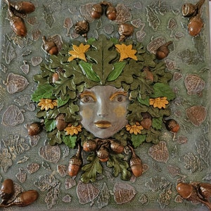 May include: A 3D mixed media artwork featuring a woman's face surrounded by green leaves, acorns, and yellow flowers. The artwork is painted on a canvas with a textured background.
