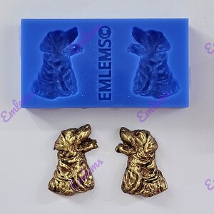 May include: Two blue silicone molds with the word "EMLEMSO" printed on the side. Each mold has a raised design of a dog's head. Two gold-colored dog head figurines are shown below the molds.