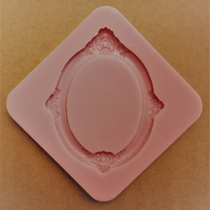 May include: Pink silicone mould shaped like an oval frame with ornate details.