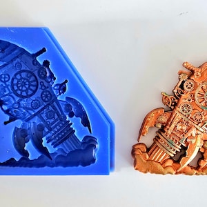 May include: A blue silicone mould with a detailed design of a steampunk rocket ship. The mould is labelled "EMILEMSO".