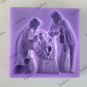 May include: Purple silicone mold with a raised design of the nativity scene. The mold features Mary, Joseph, baby Jesus in a manger, and a lamb. The mold is labeled "EMLEMSO".